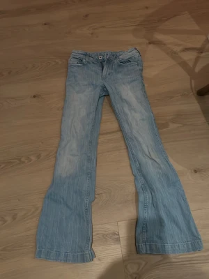 Ljusblå bootcut jeans från H&M - Säljer ett par ljusblå bootcut jeans från H&M med klassisk femficksmodell och dragkedja. Jeansen har en snygg tvättad look och är tillverkade i mjukt denimtyg. Passar perfekt till sneakers eller boots för en avslappnad vibe.