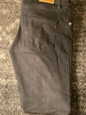 Svarta Replay jeans - Säljer ett par svarta Replay jeans i klassisk femficksmodell. Jeansen har raka ben, normal passform och är tillverkade i ett mjukt bomullsmaterial med lite stretch. Snygga detaljer med Replay-logga på fickan och metallknapp framtill.
