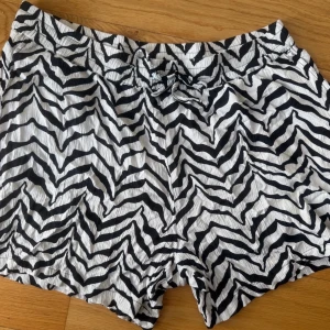 Zebramönstrade shorts med snörning - Säljer ett par riktigt snygga shorts med svartvitt zebramönster och snörning i midjan. De är tillverkade i ett lätt, skrynkligt tyg som känns luftigt och skönt. Perfekta för varma dagar när du vill sticka ut lite extra.