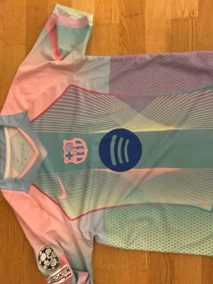 Pastellfärgad FC Barcelona x Nike tröja - Säljer en limited edition FC Barcelona x Nike tröja i pastellfärger med grafiskt mönster. Tröjan har logga från både Nike och Spotify på bröstet samt FC Barcelona-emblem. Materialet är lätt polyester och designen har inslag av ljusblått, rosa, lila och mintgrönt.