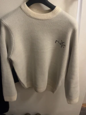 Stickad beige tröja Only & Sons NYC - Säljer en stickad beige tröja från Only & Sons med NYC-brodyr på bröstet och stor New York-text på ryggen. Tröjan har rund hals, ribbade muddar och lång ärm. Perfekt för dig som gillar streetstyle och vill ha något som sticker ut.