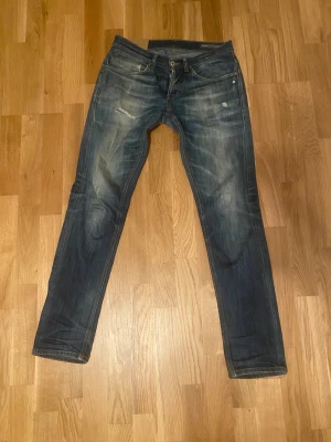 Blå jeans från dondup med slitningar - Snygga blå jeans från Dondup med coola slitningar och tvättade detaljer både fram och bak. Bädligt prominenta fades över hela byxan.Klassisk femficksmodell med slim pass form, är väligt små.
