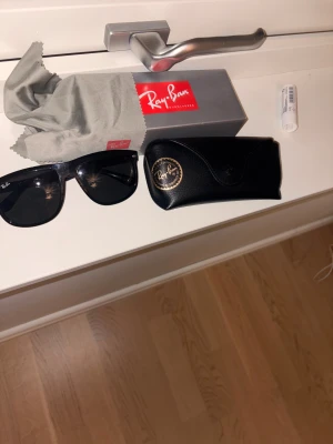 Svarta Ray-Ban boyfriend - Säljer ett par klassiska svarta Ray-Ban Wayfarer solglasögon med svart båge och mörka linser. Medföljer originalfodral i svart läder, putsduk och Ray-Ban box. Perfekt för dig som vill ha en ikonisk och stilren look.
