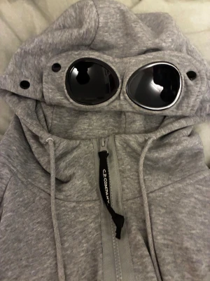  CP Company Goggle Hoodie zip - Säljer en grå hoodie från C.P. Company i storlek M med ikoniska svarta goggle-linser i huvan. Sorlek M skick 9/10. Du vet varför priset är lågt…