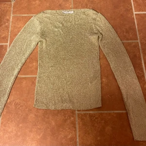 Glittrig guld långärmad topp NA-KD - Säljer en glittrig guld topp från NA-KD i storlek XS. Toppen har lång ärm, rund hals och är stickad i ett skimrande material som verkligen poppar. Andvänd enbart en gång. Perfekt för dig som vill ha något extra till din outfit. Supersnygg och trendig design!