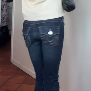 True Religion Joey Low Rise Flare Jeans -  Mörkblå jeans från True Religion, modell Joey Low Rise Flare. Snygga kontrastsömmar och ikoniska broderade fickor bak med knappar. Flare-ben och låg midja ger en retro vibe. Tillverkade i klassiskt jeansmaterial. Säljer då dem e för långa för mig har gått upp dem lite men dem är uppsydda runt 1/2 cm passar mig som e 160 men de går o ta ner de ja har sytt då är innerbenslänhden runt 84 cm