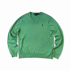 Ralph Lauren tröja - Säljer en snygg grön tröja från Ralph Lauren med v-ringning och det klassiska logotypbroderiet på bröstet. Tröjan är i bomull och har långa ärmar, perfekt för en stilren look.