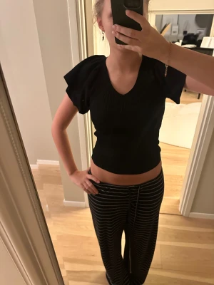 Svart ribbad topp  - Svart  topp med v-ringning och korta volymärmar. Toppen är ribbad och har öppen rygg ( men bh-n syns ej ) med knytband upptill. Perfekt för dig som gillar trendiga detaljer och en snygg siluett.