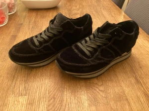 Svarta Philippe Model sneakers i mocka - Snygga svarta sneakers från Philippe Model med coola detaljer i mocka och skinn. Skorna har rund tå, platt sula med grå och vit rand, samt snörning framtill. Perfekt för dig som gillar en stilren och lyxig look med lite extra edge.