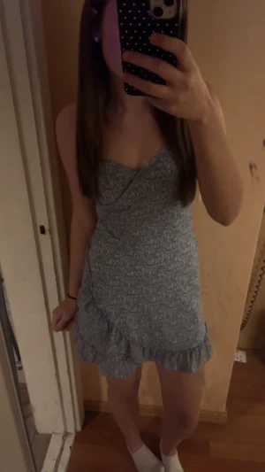 Blå blommig kort klänning med volang - Supersöt blå klänning med små vita blommor, justerbara smala axelband och volangkant nertill. Figurnära passform och kort längd, perfekt för varma dagar. Tillverkad i mjukt och lätt tyg som känns skönt mot huden.