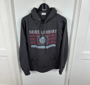 Svart Saint Laurent hoodie med tryck - Saint Laurent hoodie i nytt skick. Väldigt eftertraktad, inga defekter och funkar till mycket. Hoodien är även extremt sällsynt och säljs inte längre i butik. Allt är äkta! Hör av dig vid funderingar!😄