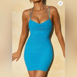 Blå tight kortklänning från Oh Polly - Supersnygg blå kortklänning från Oh Polly med smala axelband och draperad front. Klänningen har en figurnära passform, lätt rynkad effekt och dragkedja bak. Perfekt för dig som vill sticka ut med en färgstark look och visa lite hud.