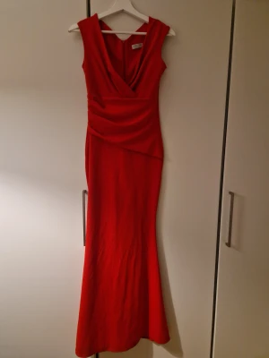 Röd långklänning från Goddiva - Snygg röd långklänning från Goddiva med omlott-detalj upptill och figurnära passform. Klänningen är ärmlös och har en dragkedja i ryggen. Perfekt för dig som vill sticka ut med en elegant och stilren look. 