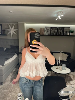 Vit volang linnetopp med smala axelband - Supersöt vit linnetopp med smala axelband och v-ringad hals. Toppen har volanger nedtill och ett luftigt, flowy tyg som ger en romantisk vibe. Perfekt till jeans eller kjol när du vill ha en chill och feminin look.