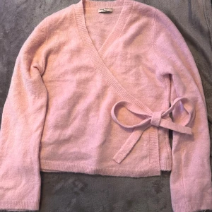 omlottkofta  Gina Tricot - Supermysig ljusrosa omlottkofta från Gina Tricot i storlek XL. Koftan har en snygg v-ringning, långa ärmar och en rosett på sidan som knyts för extra stilpoäng. Materialet är mjukt och stickat, perfekt för att hålla dig varm och comfy.