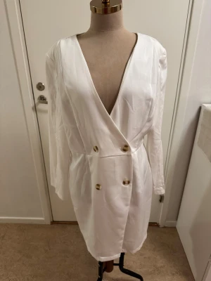 Vit omlottklänning från SHEIN XL - Snygg vit kortklänning från SHEIN i omlottmodell med djup v-ringning och långa ärmar. Klänningen har dekorativa guldknappar framtill och markerad midja. Tillverkad i ett slätt, lätt material som ger en elegant look.