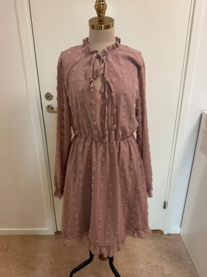 Rosa prickig klänning från SHEIN - Supersöt rosa kortklänning från SHEIN med prickigt strukturmönster, volangdetaljer vid hals och fåll samt knytning i halsen. Långärmad modell med markerad midja och lätt, flowy känsla. Perfekt för dig som gillar romantisk och trendig stil.