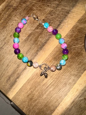 Skulle du vilja köpa ett sånt här armband gjord av kärlek skydd och trygghet? - Namn ”ecolon.ring.  Artikelnummer ”48PQ”17 cm” Unikt armband med runda pärlor i rosa, blått, grönt, lila och beige. Armbandet har en silverfärgad berlock med körsbär och ögondetalj. Lås i metall. Perfekt för dig som gillar färg och personliga smycken.