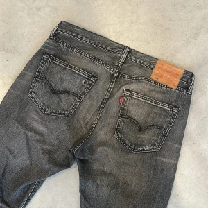 Levi's 501 - Säljer ett par vintage Levi's 501 jeans i svart tvättad denim med klassisk straight fit. Jeansen har fem fickor, knappgylf och den ikoniska läderpatchen bak. Snyggt slitna detaljer och kontrastsömmar ger en cool vintage vibe.