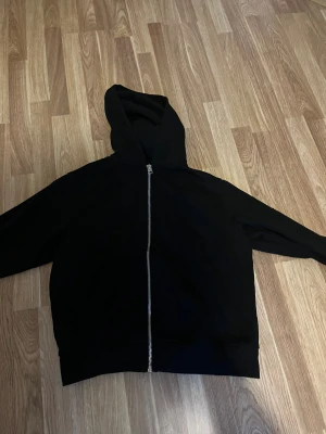 Svart hoodie med dragkedja Jack & Jones - Svart hoodie från Jack & Jones i storlek M. Klassisk modell med hel dragkedja framtill, huva och känguruficka. Tillverkad i mjukt sweatshirtmaterial, perfekt för en chill och avslappnad stil.