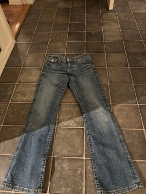 Blå bootcut jeans från Gina Tricot - Snygga blå jeans från Gina Tricot i storlek 164. Modellen har bootcut-ben och klassisk femficksdesign med en ficka med lock och knapp bak. Jeansen har kontrastsömmar och är tillverkade i slitstarkt denimtyg. Perfekt för dig som gillar retrovibbar och bekväm passform.