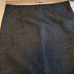 Glittrig svart kortkjol från Mystify - Snygg svart kortkjol från Mystify med glittrigt tyg som ger en cool shimmer-effekt. Kjolen har rak passform och är fodrad på insidan för extra komfort. Perfekt för dig som vill sticka ut med lite extra glitter i outfiten.