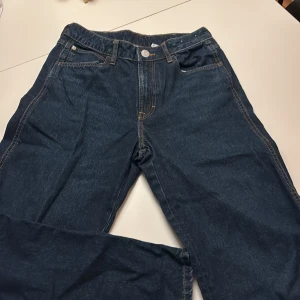Blå baggy jeans från H&M - Snygga mörkblå baggy jeans från H&M med justerbar midja. Klassisk femficksmodell med kontrastsömmar och rak passform. Perfekta för dig som gillar avslappnad stil och vill ha extra rörelsefrihet.
