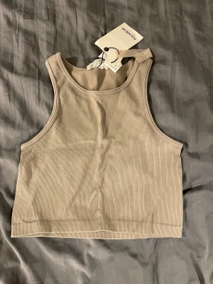 Beige ribbad linnetopp Pull&Bear - Säljer en beige ribbad linnetopp från Pull&Bear. Toppen har en croppad passform och är ärmlös med breda axelband. Perfekt för att styla med jeans eller kjol för en clean och enkel look.