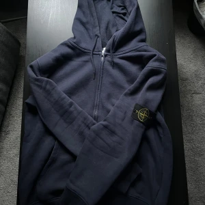 Mörkblå hoodie från Stone Island - Säljer en mörkblå hoodie från Stone Island med dragkedja och huva. Klassisk patch på vänster ärm och justerbara snören i huvan. Tillverkad i mjuk bomull, 