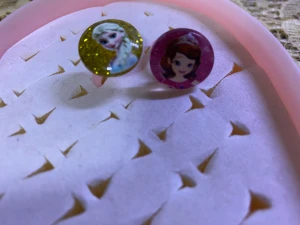 Glittriga Disney-ringar Elsa & Sofia - Två färgglada barnringar med motiv av Elsa från Frost och prinsessan Sofia. Ena ringen har guldfärgad glitterbakgrund, den andra rosa. Båda är gjorda av plast och har rund form med glansig yta. Perfekt för dig som älskar Disneyprinsessor och vill ha något extra till din outfit. 35kr/2st/bild 