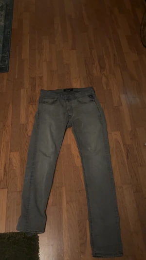 Replay anbass gråa  - Snygga grå jeans från Replay med klassisk femficksdesign och raka ben. Jeansen har mörkgrå ton, diskreta slitningar och tydliga sömmar på bakfickorna. Passar dig som gillar stilrena och tidlösa jeans med bra passform.