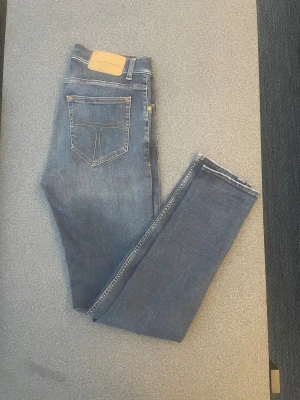 Tiger of Sweden Evolve jeans blå 29/32 - Snygga blå jeans från Tiger of Sweden, modell Evolve. Klassisk femficksdesign med guldfärgade sömmar och läderpatch bak. Smal passform och raka ben, tillverkade i mjukt jeanstyg. Perfekt för dig som gillar stilrena och moderna jeans.         Pris kan diskuteras!!