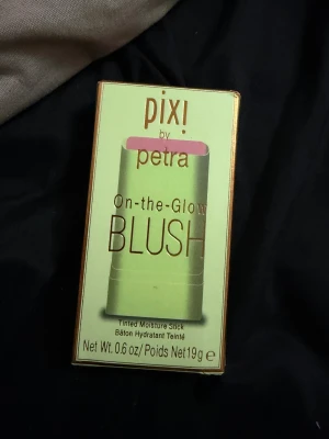 Pixi On-the-Glow Blush Fleur - On-the-Glow Blush från Pixi i färgen Fleur är en solid blush-stick med återfuktande formula. Den har en ljusrosa ton och innehåller ginseng, aloe vera och fruktextrakt. Kan användas på både kinder och läppar för en naturlig glow. Förpackningen är grön med rosa detaljer.