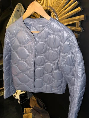 Grå quiltad pufferjacka från MNG - Säljer en grå pufferjacka från MNG i storlek M. Jackan har ett unikt quiltat mönster med rundade former, knäppning framtill och långärmade. Materialet är glansigt syntet och jackan har en clean, modern look som är lätt att styla till olika outfits.