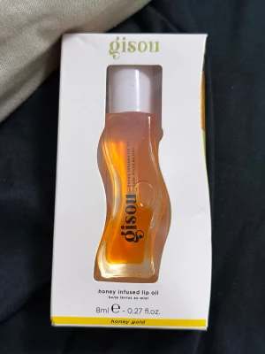 Gisou Honey Infused Lip Oil - Gisou Honey Infused Lip Oil i färgen honey gold, 8 ml. Kommer i en snygg vågformad genomskinlig flaska med vit kork. Oljan är gyllene och innehåller honung, propolis och naturliga oljor som ger läpparna glans och mjukhet. Perfekt för dig som vill ha återfuktade och glansiga läppar.
