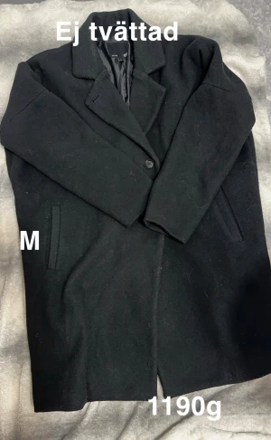 Svart klassisk kappa, stl M - Stilren svart kappa med klassisk krage och knäppning framtill. Jackan har två fickor på sidorna. Perfekt för dig som gillar en tidlös look och vill hålla dig varm under kyliga dagar.🌸 Fint använt skick. Ej tvättad. Storlek M