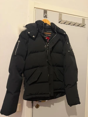  Moose Knuckles jacka  - Svart pufferjacka från Moose Knuckles med vit päls på huvan, snygga detaljer som dragkedjor på ärmarna och logopatch på armen. Kvitto medföljer skriv vid minsta fundering 