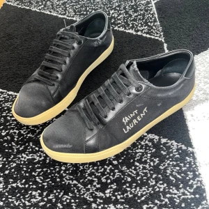 Svarta Saint Laurent sneakers strl 41 - Svarta sneakers från Saint Laurent med handskriven logga på sidan. Skorna har svart canvas och skinn, svarta snören och beige sula. Klassisk låg modell med rund tå och platt sula. Tillverkade i Italien, stilrena och passar perfekt till streetwear. Storlek 41 och är i bra skick! Ända defekterna är att slitningen som ni ser på bild 5 har blivit öppnad lite men det är självklart inget hål. Och så är sulan lite mer beige/gula än normalt. Annars jättefina! Ingen box men dustbag ingår