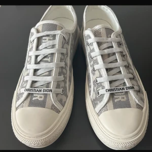 Sneakers från Christian Dior - Snygga sneakers från Christian Dior i grått och vitt med ikoniskt Dior-mönster. Skorna har snörning, platt sula och tydlig logga både på sidan och baktill. Hör av er vid frågor eller fler bilder💕aldrig använda!! Säljer pga har för många skor. Passar strl 39-40 