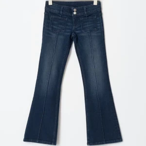 Mörkblå bootcut jeans med fickor - Snygga mörkblå jeans med bootcut passform och markerade sömmar framtill. Byxorna har två stora fickor fram och dubbla knappar i midjan. Perfekta för dig som gillar en retroinspirerad look.