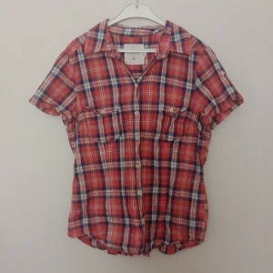 Röd rutig skjorta från H&M L.O.G.G. - Kortärmad röd rutig skjorta från H&M L.O.G.G. med blå och vita detaljer. Skjortan har två bröstfickor med knappar och klassisk krage. Tillverkad i mjuk bomull, perfekt för en avslappnad och cool stil.