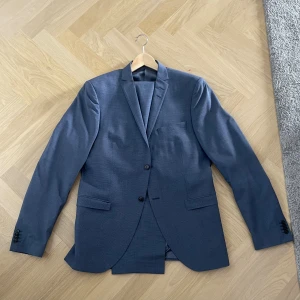 Mörkblå kavaj från tiger of Sweden - Snygg mörkblå kavaj med klassisk passform och två knappar framtill. Kavajen har dubbla sprund bak, fickor med lock och en bröstficka. Tillverkad i en tunn ullmix som ger en stilren look. Perfekt för dig som vill ha en clean och tidlös stil. Storlek 152. Kommer med byxorna.