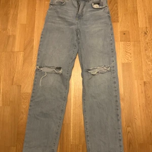 Ljusblå slitna jeans med hål på knäna - Ljusblå jeans med raka ben och snygga slitningar över båda knäna. Jeansen har klassisk femficksdesign och är tillverkade i robust denim. Perfekta för en avslappnad och trendig look.