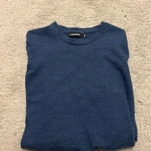 Blå stickad tröja från J.Lindeberg - Mysig blå stickad tröja från J.Lindeberg med rund halsringning och diskret JL-logga på bröstet. Tröjan har långa ärmar och ribbade muddar vid ärmslut och nederkant. Perfekt för lager-på-lager under kyliga dagar. Tröjan passar dig som är 165 ung. 