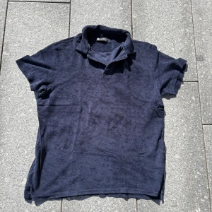 Mörkblå frotté t-shirt från Morris - Snygg mörkblå t-shirt från Morris i frottématerial. Modellen har korta ärmar och en klassisk krage som ger en chill och sportig vibe. Perfekt för dig som gillar en lite unik och mjuk känsla på din t-shirt.