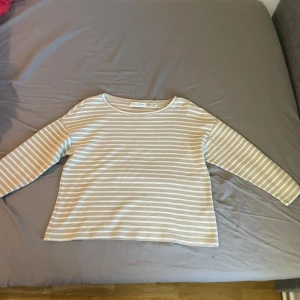Randig beige långärmad tröja Marc O'Polo - Superfin långärmad tröja från Marc O'Polo i beige och vitt med klassiskt randigt mönster. Tröjan har en rak passform och rund halsringning, perfekt för en avslappnad och stilren look. Tillverkad i mjuk bomull för extra komfort.