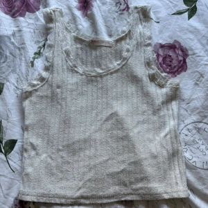 Vit ribbad linnetopp med spetskant - Supersöt vit ribbad linnetopp från Shein med spetsdetaljer runt halsringning och ärmhål. Toppen är ärmlös och har en figurnära passform som framhäver siluetten. Perfekt att styla med jeans eller kjol för en fräsch look.