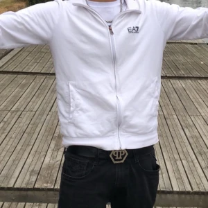 Vit zipjacka från EA7 Emporio Armani - Fräsch vit jacka från EA7 Emporio Armani med hel dragkedja framtill och diskret logga på bröstet. Jackan har en clean look, ståkrage och två fickor på sidorna. Perfekt för dig som gillar stilren och sportig vibe. OBS!! NY pris 1000kr