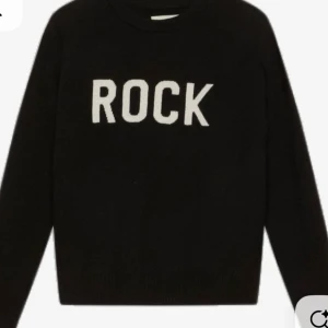 Svart stickad tröja med ROCK-tryck - Svart stickad tröja med vit text 'ROCK' framtill. Klassisk rund halsringning och långa ärmar. Perfekt för dig som vill ha en enkel men cool statement-tröja i garderoben.