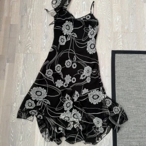 Svart blommig klänning Collection - Supersnygg svart klänning med vita blommor från Collection Debenhams. Klänningen har asymmetrisk nederkant, smala axelband och ett coolt blommönster. Tillverkad i 100% polyester och har en lätt, flowy känsla. 